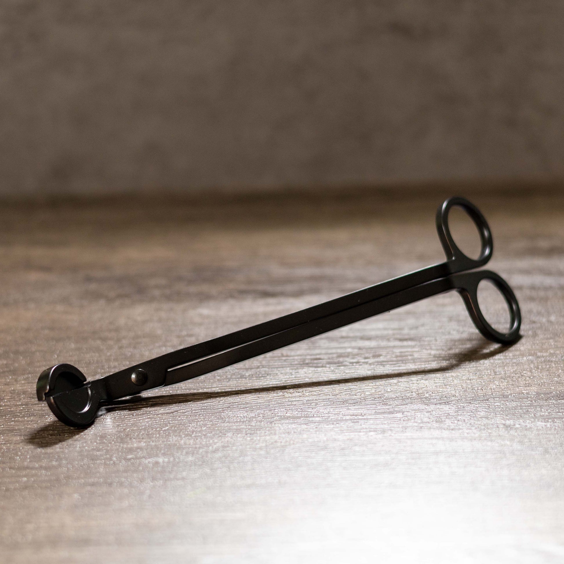 Black metal wick trimmer on a wooden surface with a blurred background