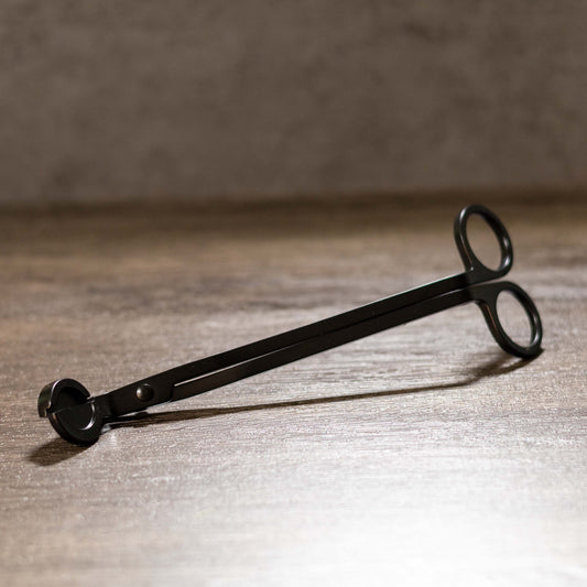 Black metal wick trimmer on a wooden surface with a blurred background