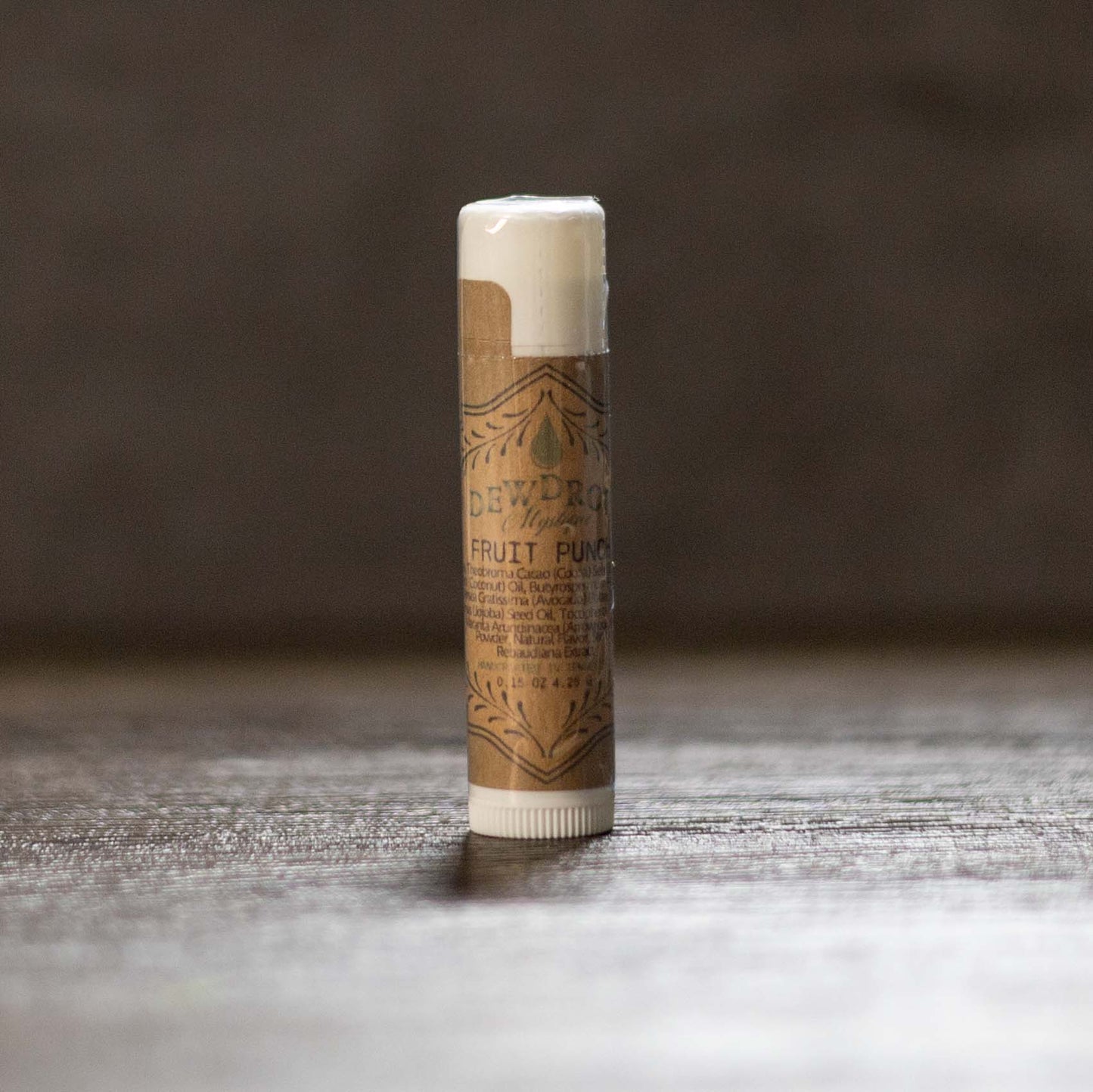 Fruit punch lip balm tube with a brown label on a wooden surface.