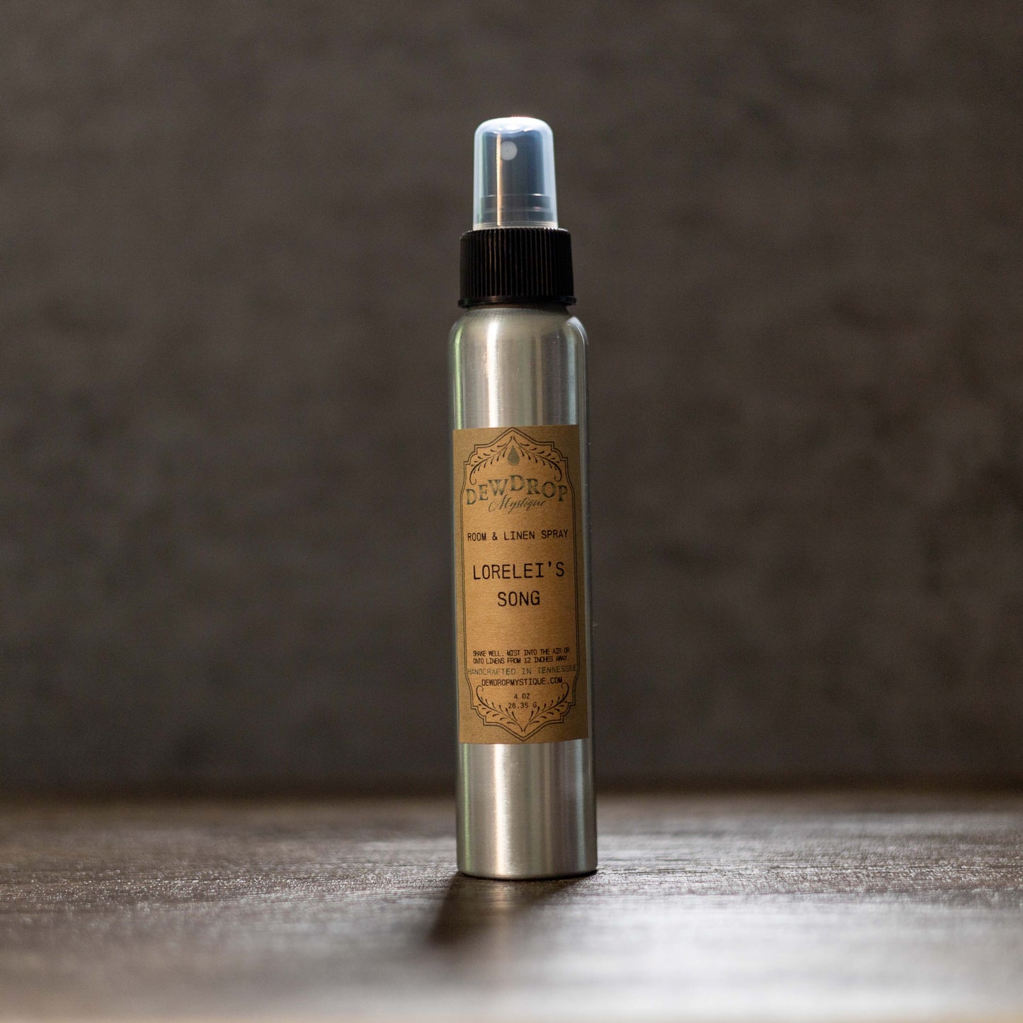 Metallic spray bottle with a brown label on a wooden surface and dark background