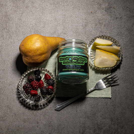 A Pear and Berry Oasis candle jar placed on a grey surface, surrounded by an pear, sliced pears, and a fork, creating an aromatic setting.
