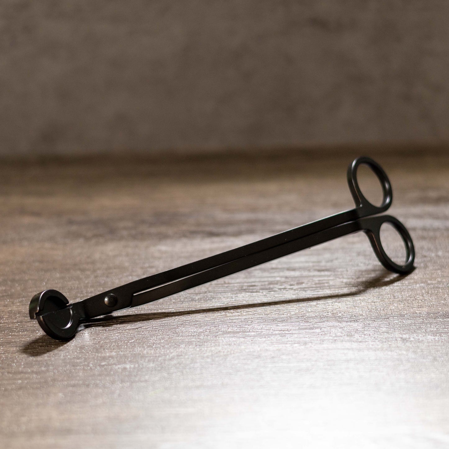 Black metal wick trimmer on a wooden surface with a blurred background