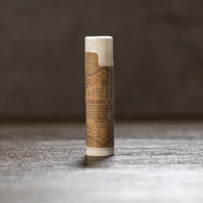 Balm stick with brown paper wrapper on a wooden surface