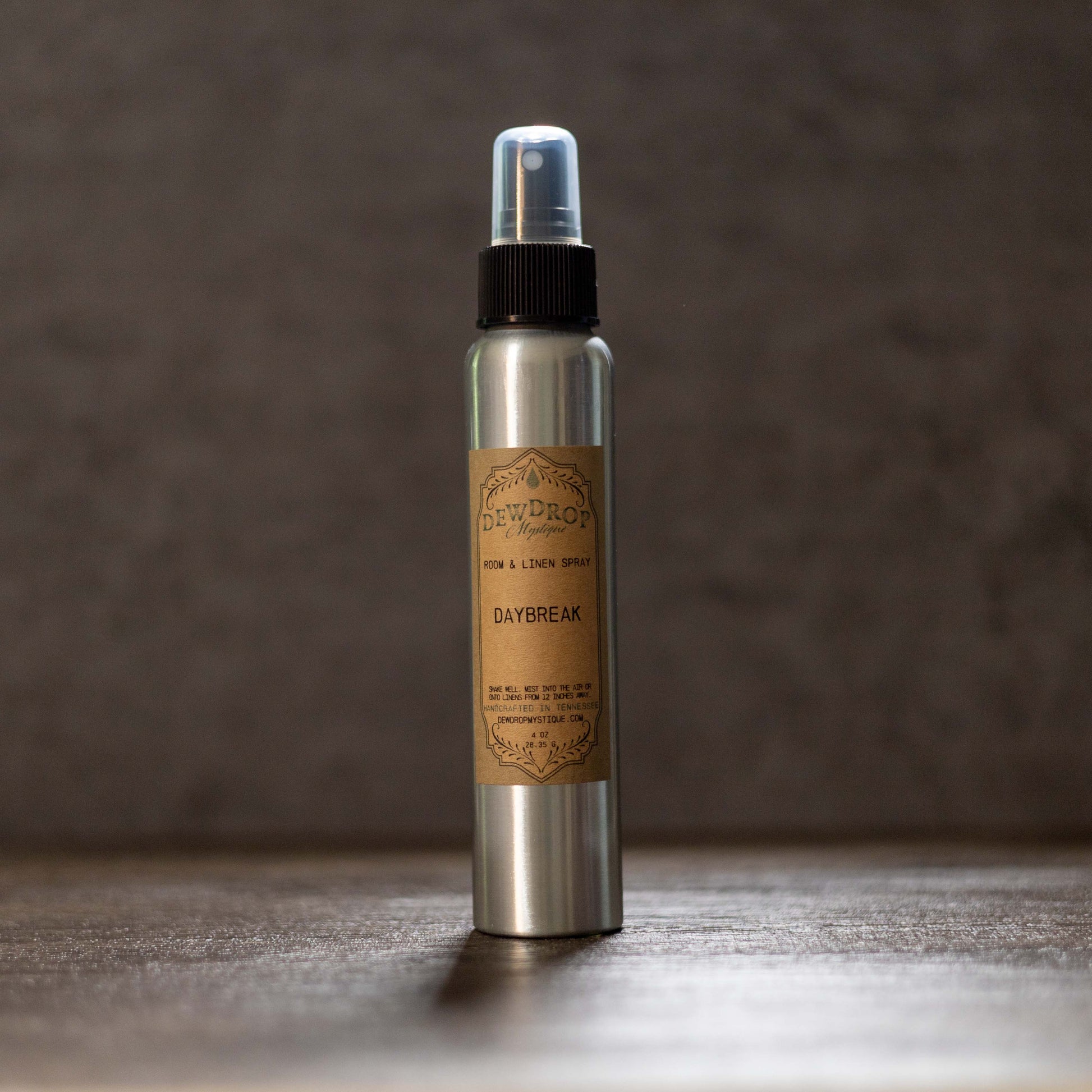 Metallic spray bottle with a brown label on a wooden surface and dark background