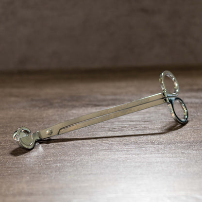 Silver wick trimmer on a wooden surface.