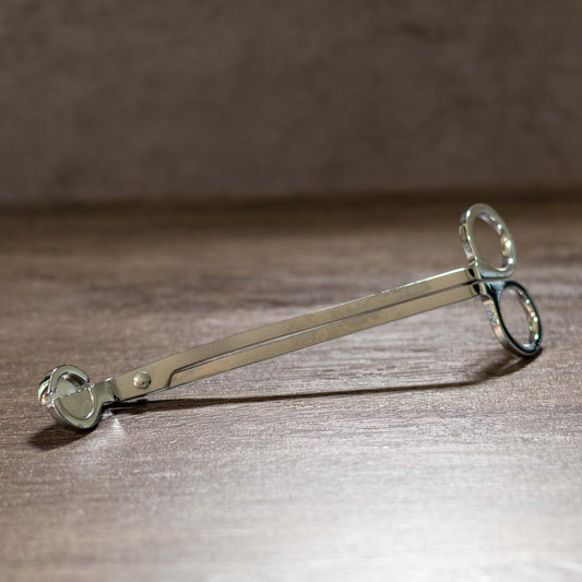 Silver wick trimmer on a wooden surface.